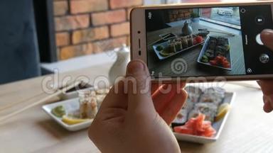 青少年的手在智能手机上制作食物的照片。 背景上日本料理的寿司卷